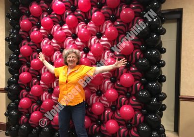 Custom balloons wall in white, red, & black behind former owner Christine Maentz