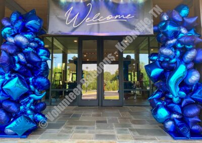 Giant blue balloon garlands surrounding an entrance, with a "welcome" banner on top