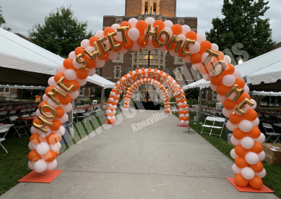 3 balloon arches in orange and white lining a pathway between pavillons, each balloon arch with a line from the song "Rocky Top"