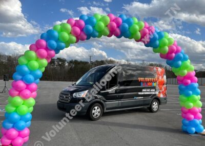 Large balloon arch in neon pink, neon green, and neon blue with the Volunteer Balloons Delivery van under it