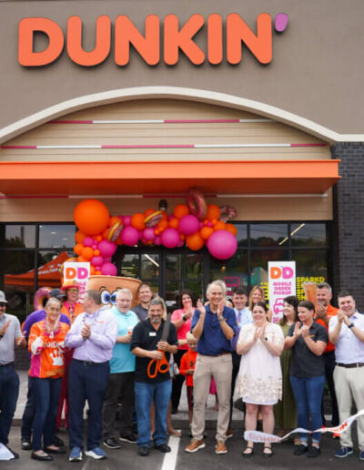 Organic balloon garland in dunkin logo colors with jumbo donut foils outside of entrance with large crowd gathered in front