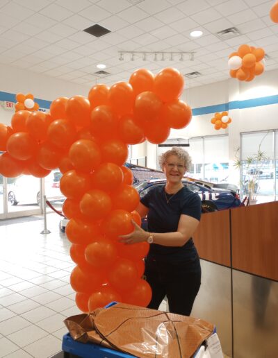 Business owner holding Power T in dealership showroom with white and orange clusters hanging behind her.