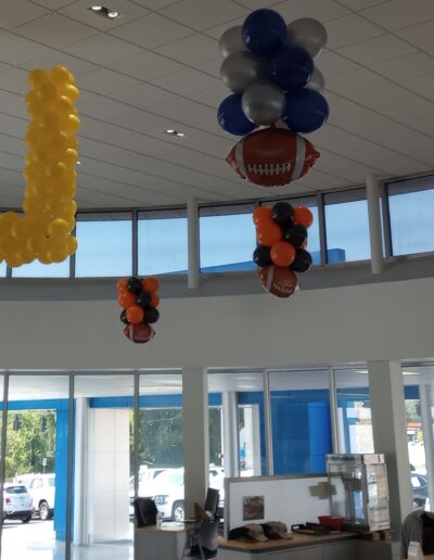 Football goal post and floating balloon columns in orange, black, blue, and silver hanging from ceiling