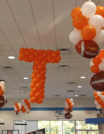 Floating balloon columns in white and orange with Footballs and orange Power T on ceiling at dealership